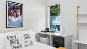 A modern bedroom with a Star Wars poster, a bed with white bedding, a window with blinds, a coffee maker, a toaster, and a black suitcase. - Leia's Rebel Princess Suite (Seattle)