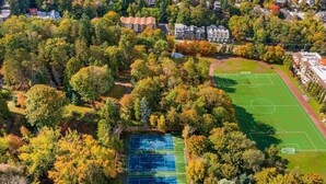 Vista aérea de una zona residencial con una cancha de tenis rodeada de árboles y casas.