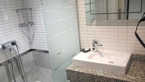 Et moderne badeværelse med et glasafskærmet brusebad, en hvid vask og et stort spejl.