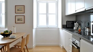 A modern kitchen with white cabinets, a wooden dining table, and a window. - Alfama Prime II by Homing (Lisbon)