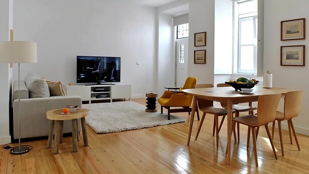 A modern living room with a flat-screen TV, a sofa, a dining table with chairs, and a small side table. - Alfama Prime II by Homing (Lisbon)