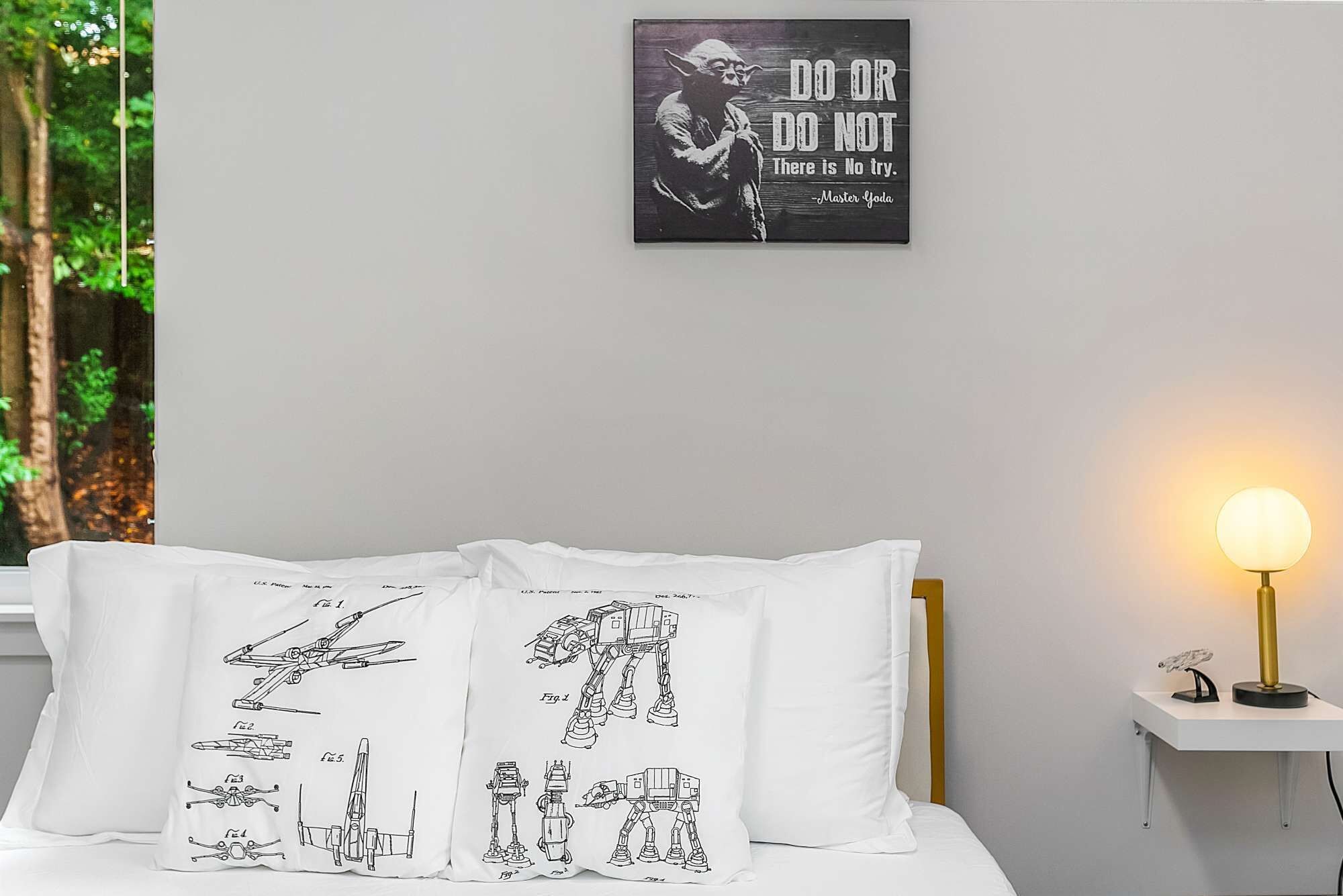 Et soveværelse med en seng, hvide puder med Star Wars-motiver, en sengetavle og et billede på væggen.