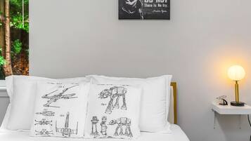 Et soveværelse med en seng, hvide puder med Star Wars-motiver, en sengetavle og et billede på væggen.
