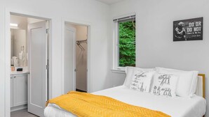 A bedroom with a bed, white pillows, a yellow throw, a Star Wars poster, and a window with a green view.