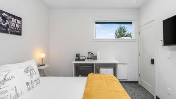 Een hotelkamer met een bed, een bureau met een computer, een raam met uitzicht op bomen en een aan de muur bevestigde televisie.