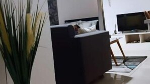 A living room with a sofa, a TV, and a plant. - Grand Studio (Abidjan)