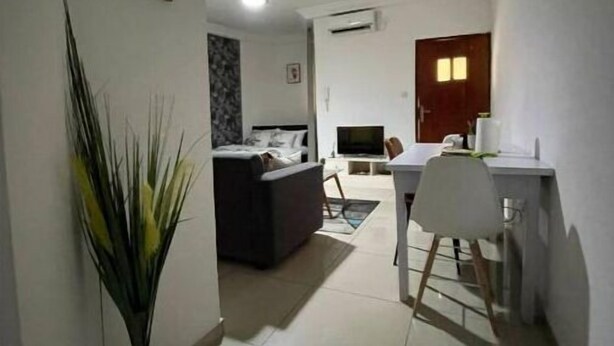 A hallway leading to a living room with a sofa, a TV, and a dining area with a table and chairs. - Grand Studio (Abidjan)