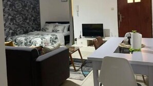 A compact hotel room with a bed, a small sofa, a TV, and a dining area with a table and chairs. - Grand Studio (Abidjan)