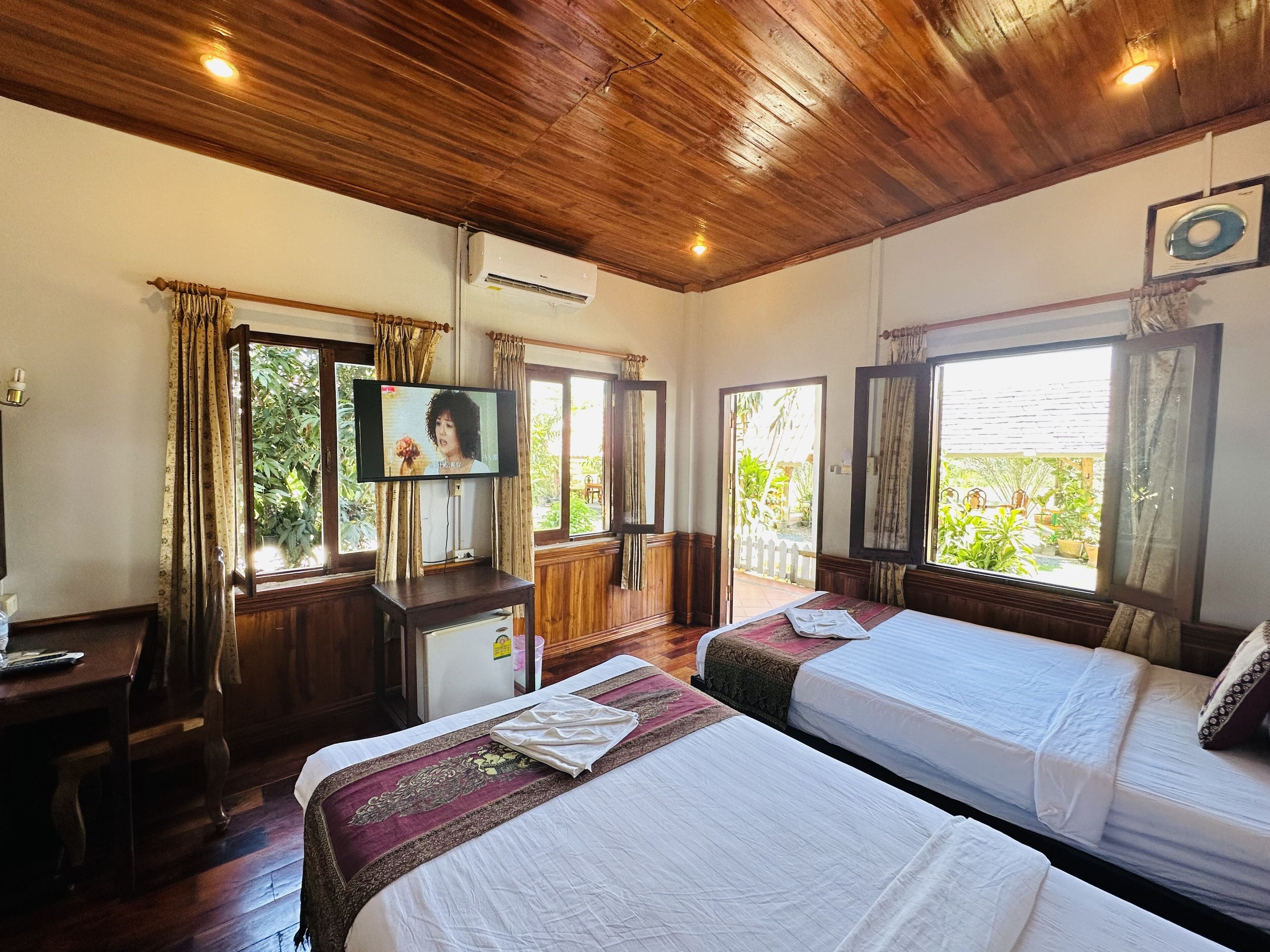 Une chambre d’hôtel avec un plafond en bois, deux lits, une télévision et de grandes fenêtres avec des rideaux.