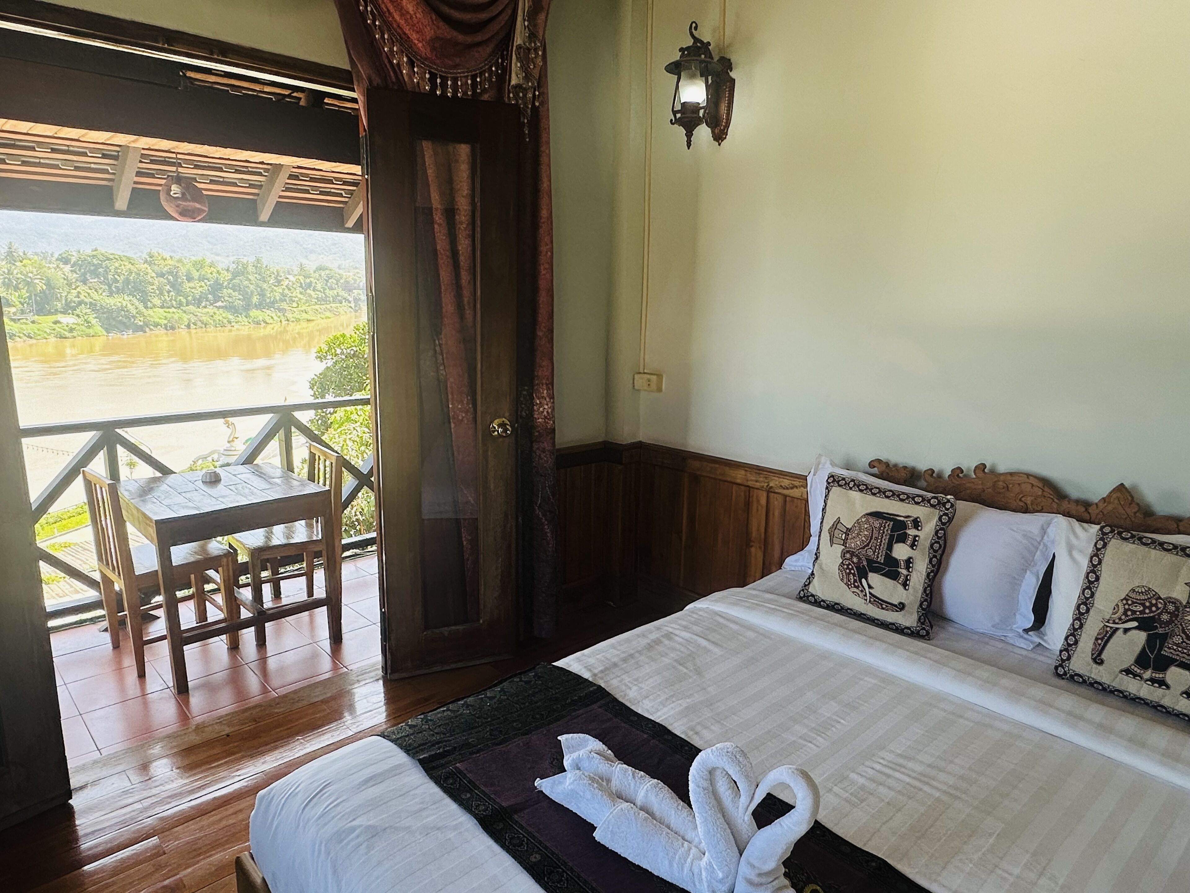 A hotel room with a bed, a table, and a chair near a window overlooking a river.