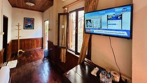 A hallway with wooden flooring, a television mounted on the wall, and a door with patterned curtains. - Kingkham Riverside Hotel (Luang Prabang)