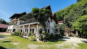 A white building with a balcony, surrounded by greenery and a clear sky. - Kingkham Riverside Hotel (Luang Prabang)