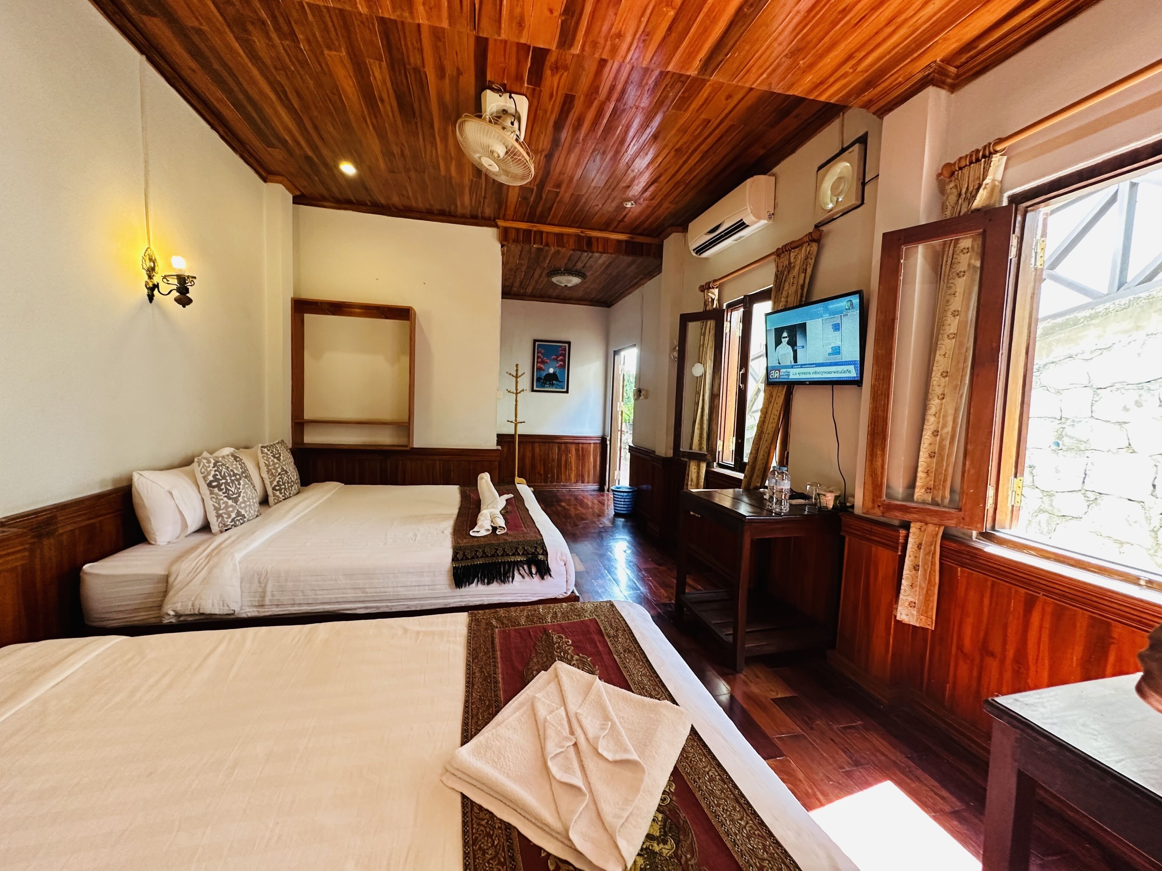 Habitación de hotel con dos camas, techo de madera, televisor y ventana con cortinas.