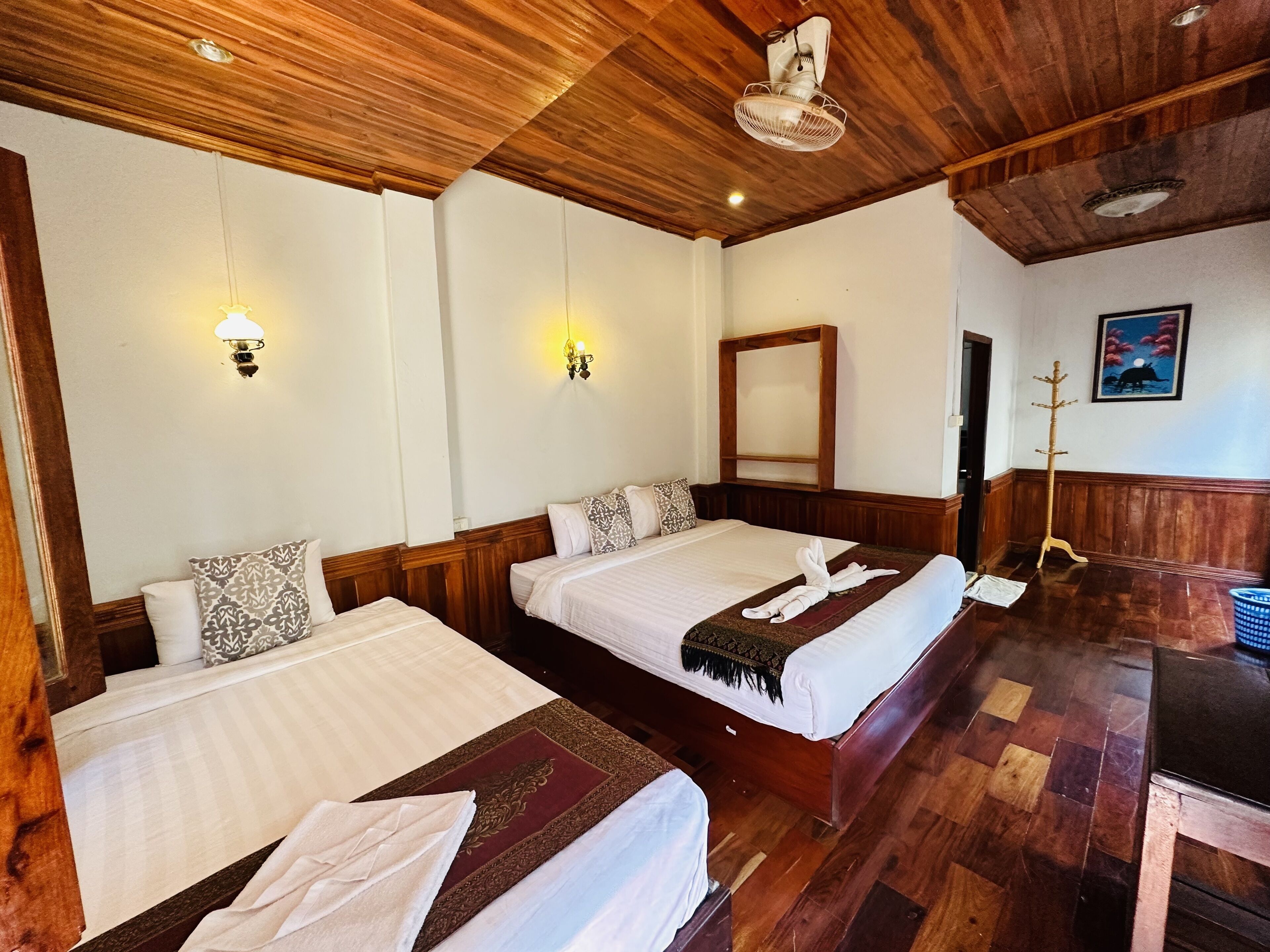 Habitación de hotel con dos camas, suelo de madera, techo de madera e iluminación empotrada en la pared.