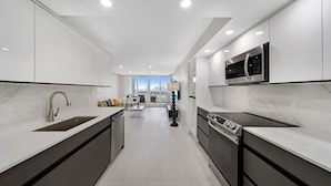 A modern kitchen with white cabinetry, a stainless steel sink, and a built-in microwave. - Bayfront High-Rise Condo | Oceanview | StayCozy (Miami)