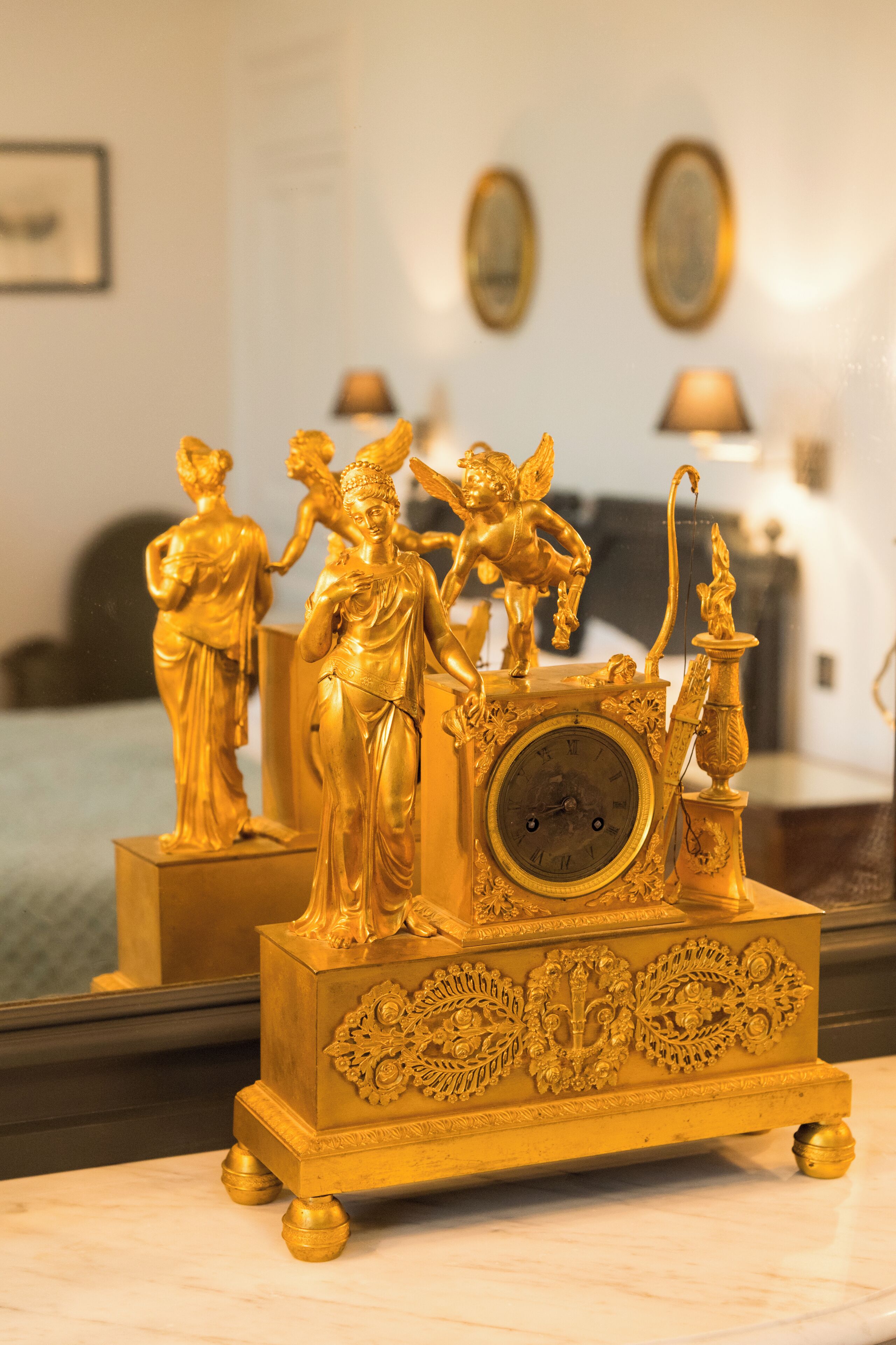 A golden clock with intricate designs and statues on top, placed on a marble surface.
