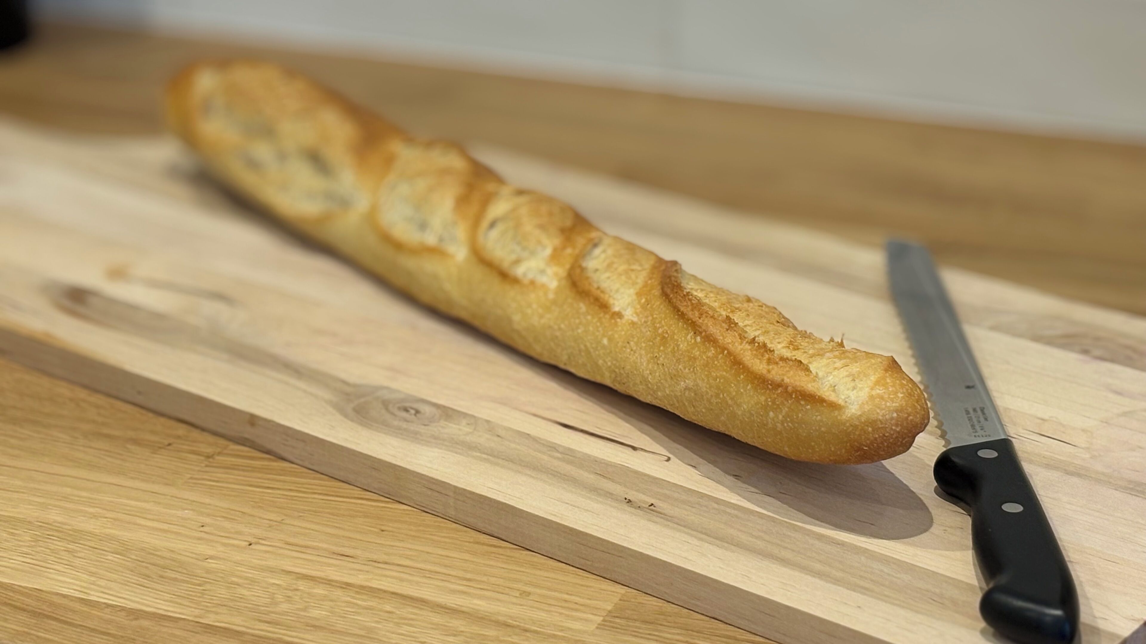A baguette on a wooden cutting board with a knife beside it.