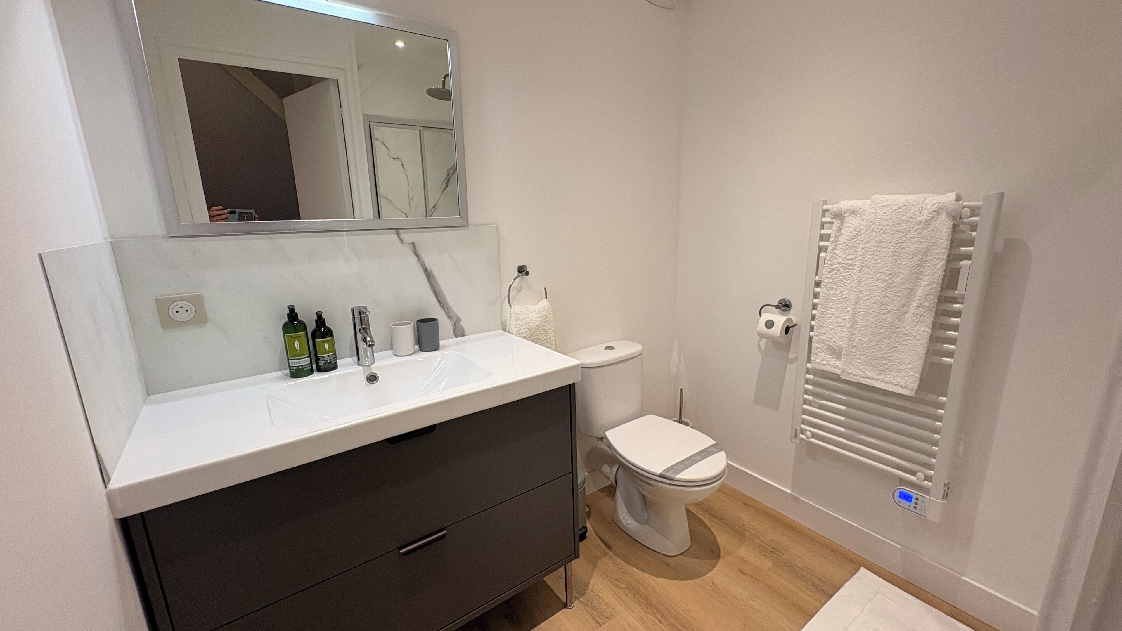A modern bathroom with a white sink, dark cabinet, and a toilet.
