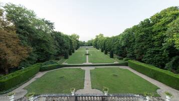 A symmetrical garden with a central pathway, bordered by neatly trimmed hedges and trees.