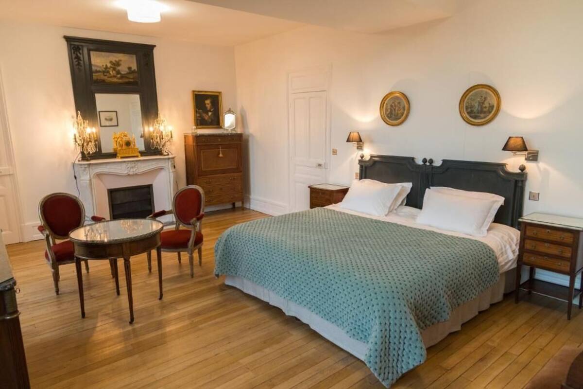 Un dormitorio con cama, chimenea, una mesa y sillas.