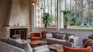 A modern living room with a fireplace, comfortable seating, and large windows overlooking a garden. - Château du Rondon (Olivet)
