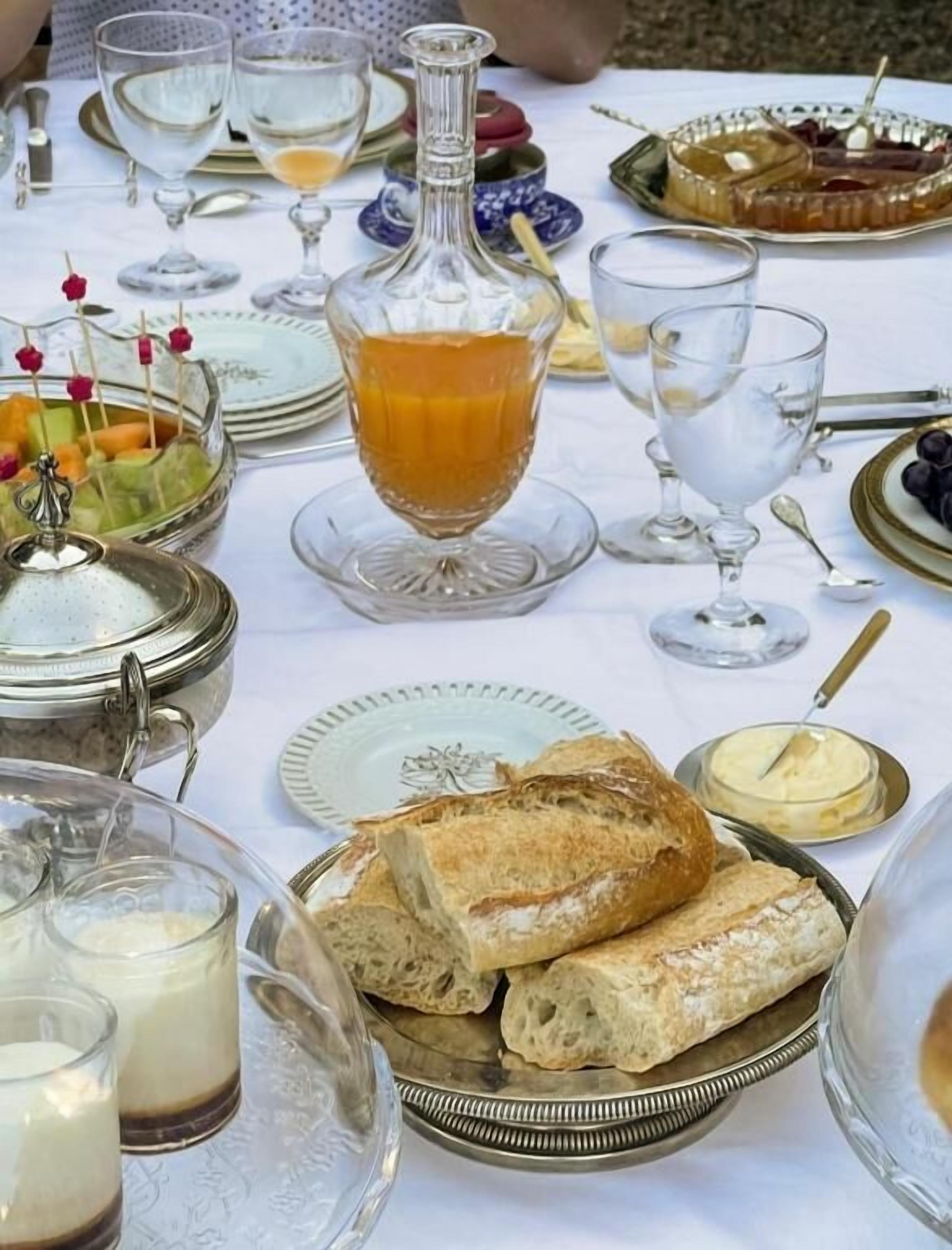 Uma mesa posta com diversos alimentos e bebidas, incluindo pão, doces e uma garrafa de suco.