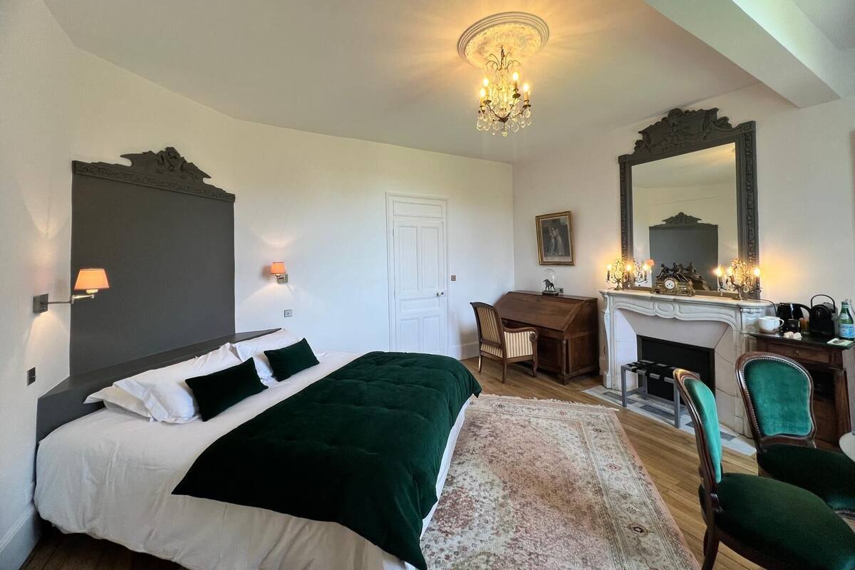 Un dormitorio con cama, escritorio, silla, chimenea y un espejo grande.