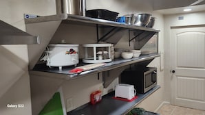 Une cuisine équipée d’un four à micro-ondes, d’un grille-pain et de divers ustensiles de cuisine rangés sur des étagères.