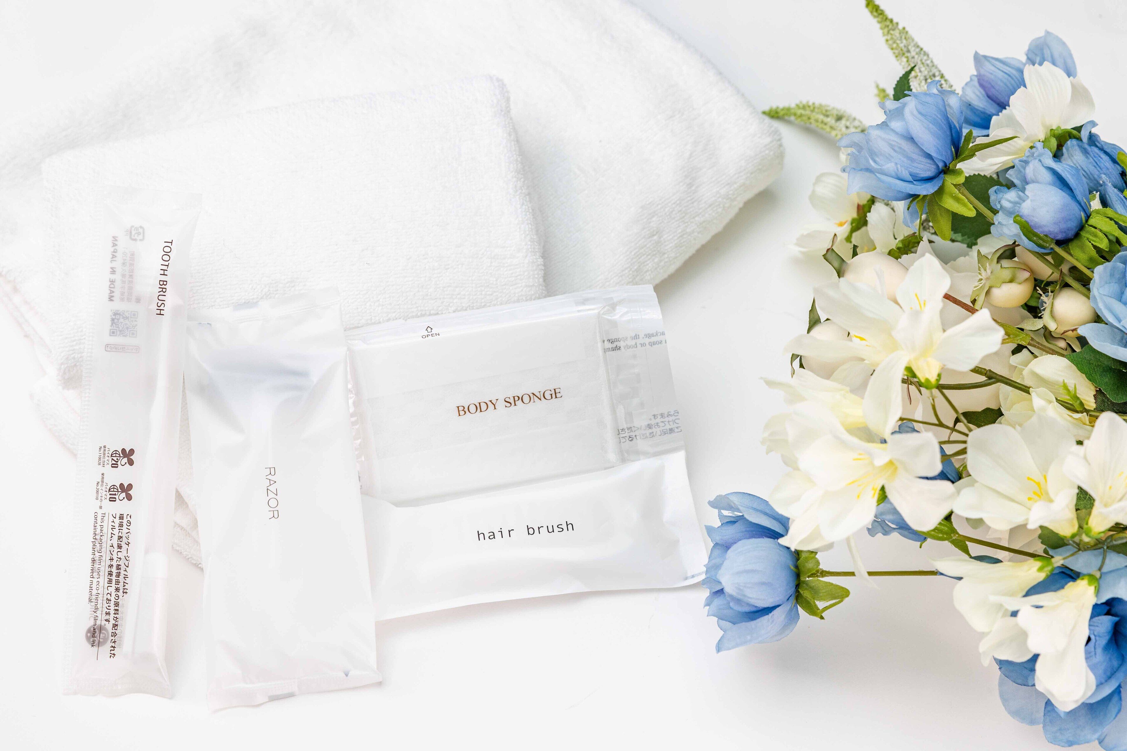 A white towel, a body sponge, and a hair brush on a white surface with blue and white flowers.