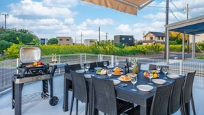 Un espacio exterior para comer con una parrilla, mesa puesta con platos, vasos y botellas.