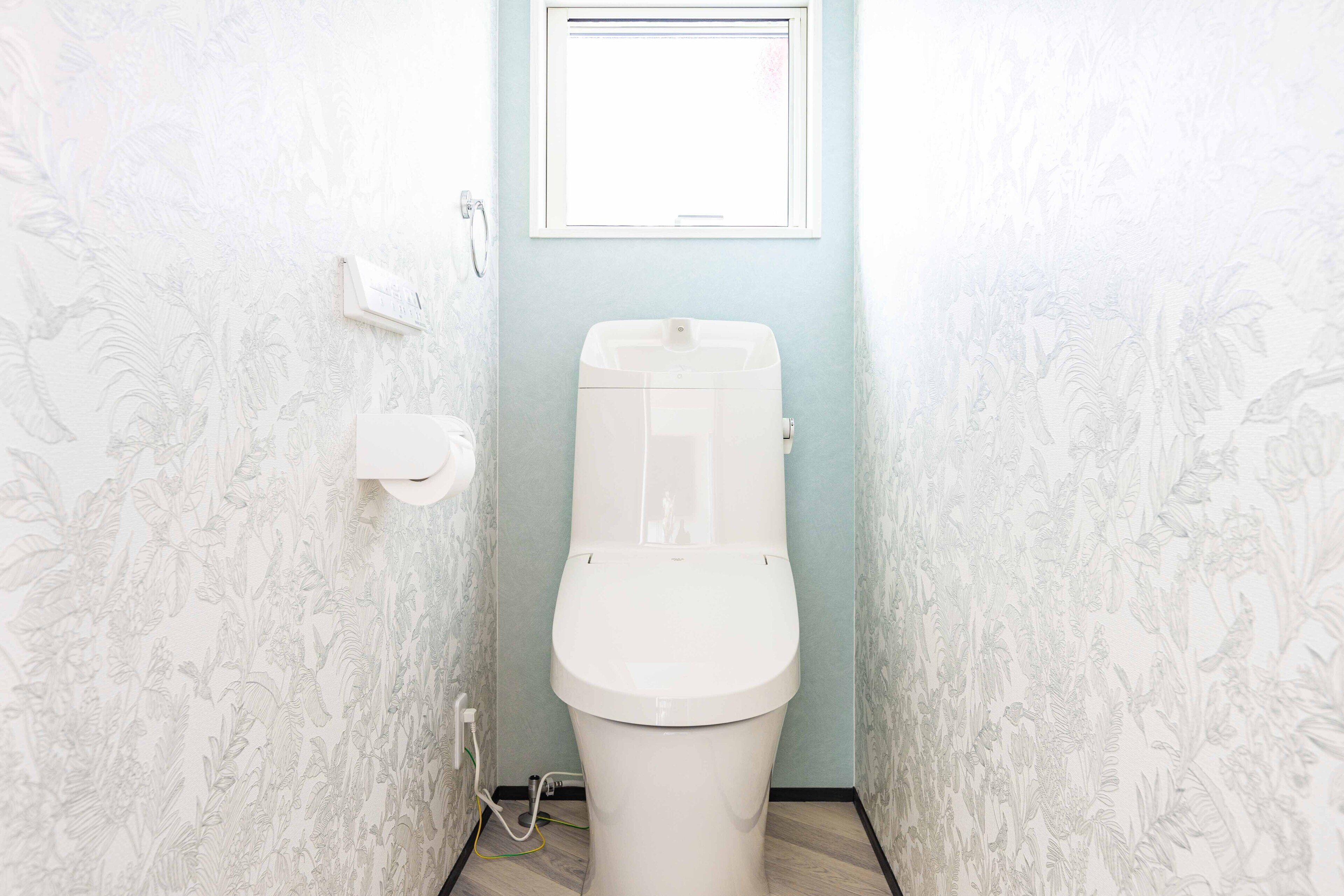 A toilet in a bathroom with floral wallpaper and a window above it.