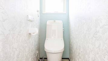 A toilet in a bathroom with floral wallpaper and a window above it.