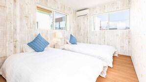 Habitación de hotel con dos camas, ropa de cama blanca, almohadas azules, una mesita de noche con lámpara y ventana con vistas.