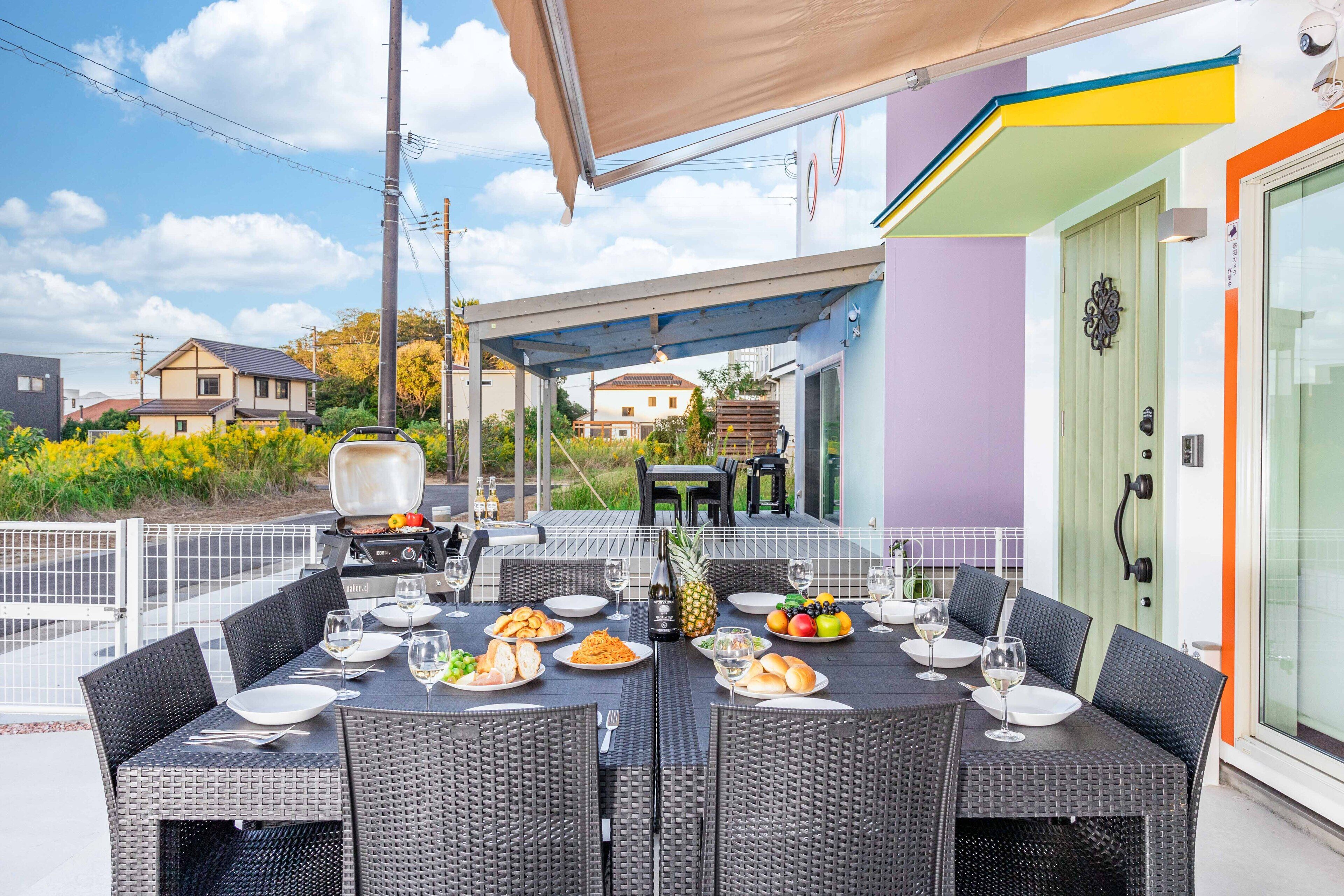 An outdoor dining area with a covered table, wicker chairs, and a grill.