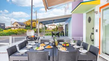 An outdoor dining area with a covered table, wicker chairs, and a grill.