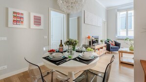 A dining area with a round table, chairs, and a chandelier. There are framed pictures on the wall and a window with blinds. - Miss Penny in Lucca With 2 Bedrooms and 1 Bathrooms (Lucca)