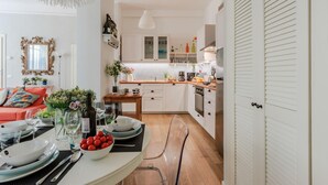A modern kitchen with white cabinets, a dining table set with plates, glasses, and a bowl of fruit. - Miss Penny in Lucca With 2 Bedrooms and 1 Bathrooms (Lucca)
