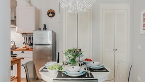 A dining area with a round table set for four, surrounded by chairs. A refrigerator and a kitchen counter with various items are visible in the background. - Miss Penny in Lucca With 2 Bedrooms and 1 Bathrooms (Lucca)