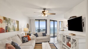 A living room with a sofa, a coffee table, a TV, and a balcony with a view. - Beachfront 1BR @ Phoenix III • Sleeps 4 • Stunning Views, Balcony, Pools & Beach Access (Orange Beach)