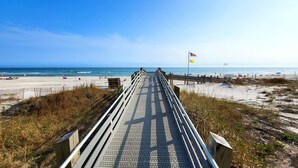 A wooden boardwalk leading to a beach with a flag and a flagpole. - Beachfront 1BR @ Phoenix III • Sleeps 4 • Stunning Views, Balcony, Pools & Beach Access (Orange Beach)