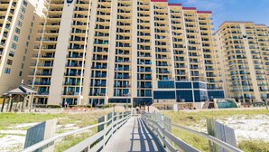 A high-rise hotel with multiple balconies, a swimming pool, and a beach view. - Beachfront 1BR @ Phoenix III • Sleeps 4 • Stunning Views, Balcony, Pools & Beach Access (Orange Beach)