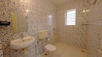 Un baño con inodoro, lavamanos y zona de ducha, con paredes y suelo de baldosas.