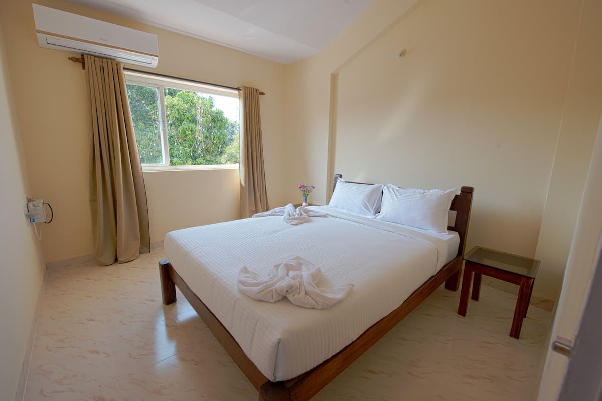 A neatly made bed with white linens, a wooden headboard, and a small bedside table with a vase of flowers.