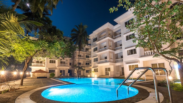 Una piscina rodeada por un edificio con balcones, palmeras y un cielo nocturno.