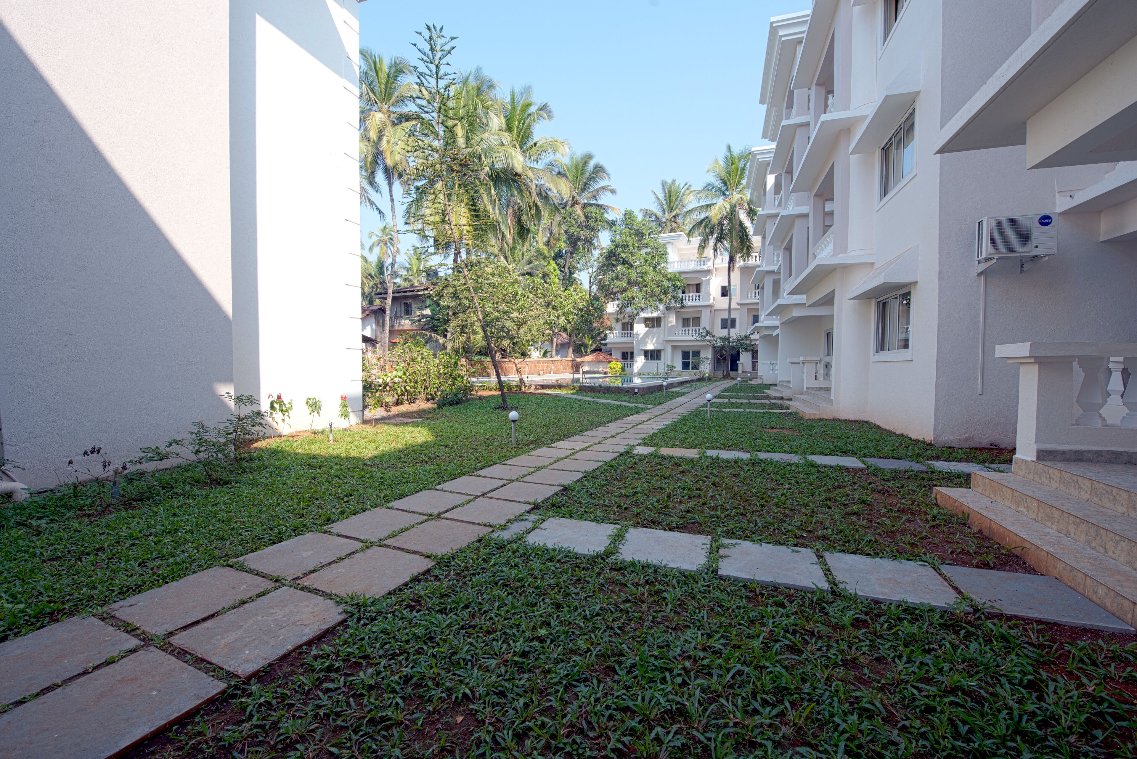 A pathway leading to a building with multiple balconies and palm trees.