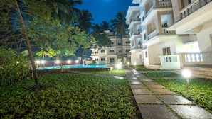 Un hotel con piscina, palmeras y cielo nocturno con luna visible.