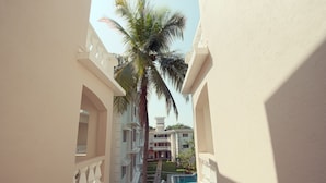 Un pasillo con piscina, palmeras y un edificio con balcones.