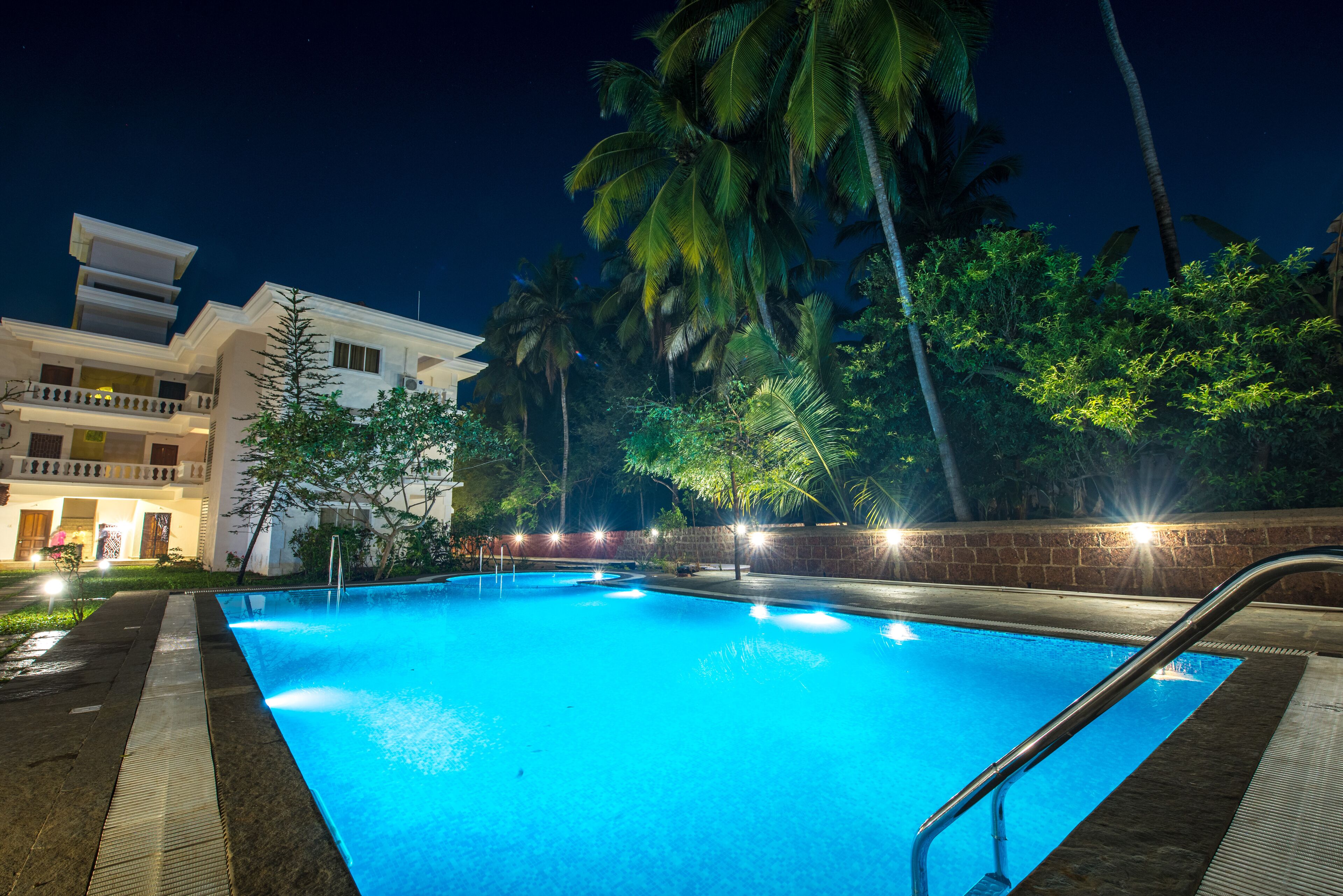 Piscina nocturna con vista a un edificio y palmeras.