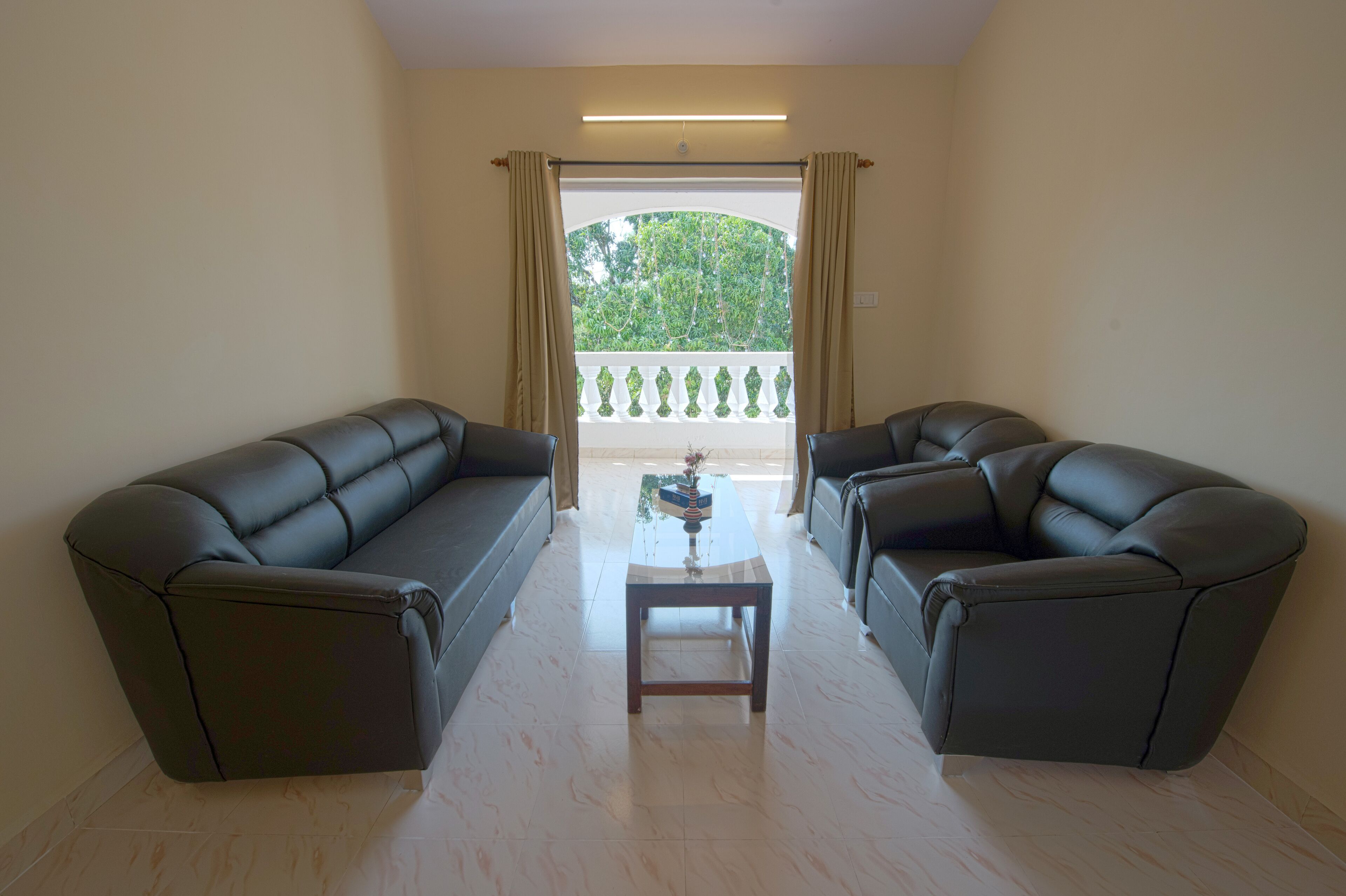 Sala de estar con dos sofás de cuero oscuro, una mesita de madera y vistas a una barandilla blanca y follaje a través de puertas de balcón.