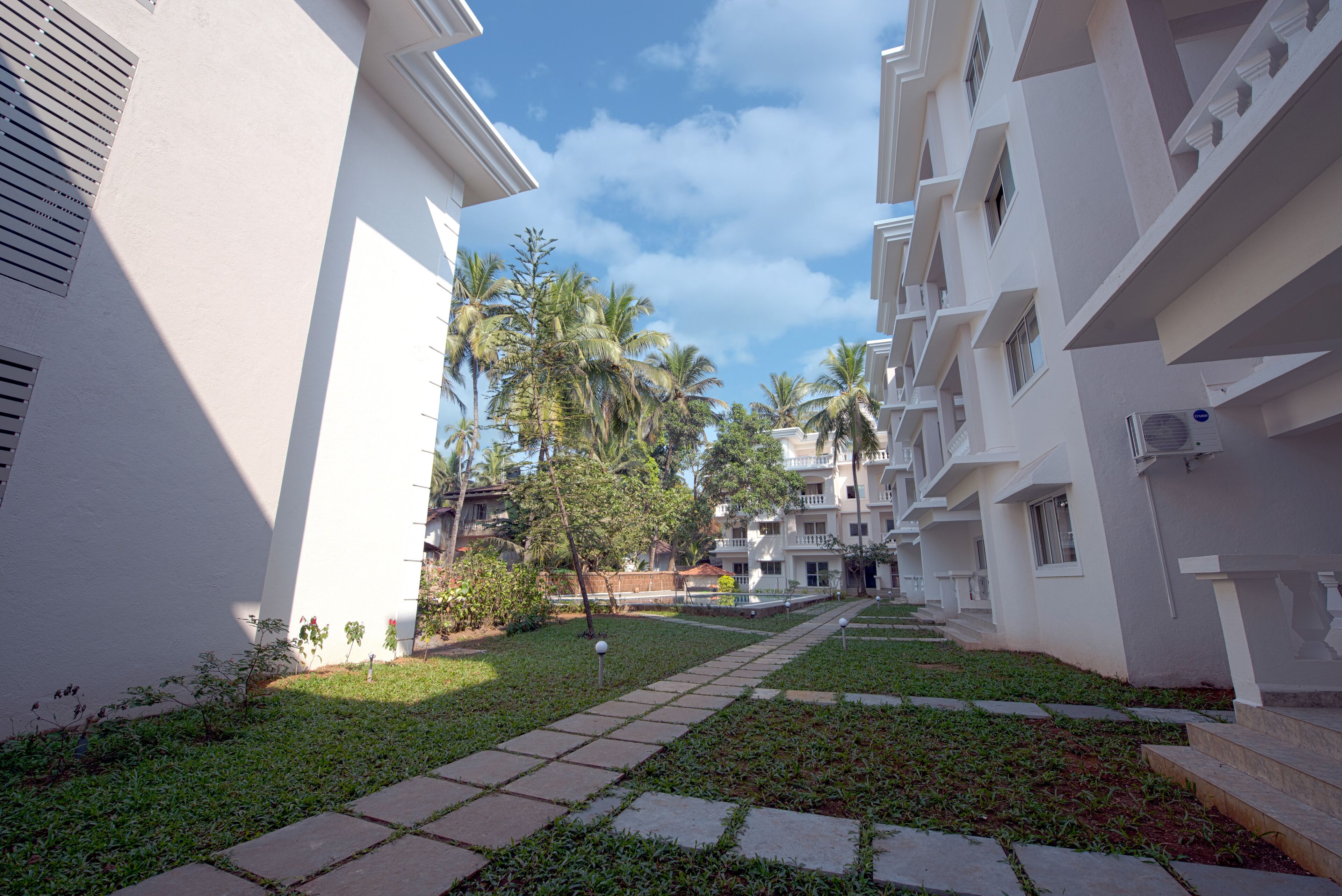 A pathway leading to a building with balconies, surrounded by greenery and palm trees.
